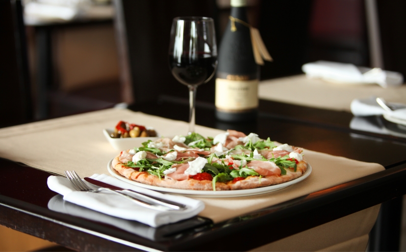 A dinner setting with pizza, a bottle of wine, and a glass filled with red wine.