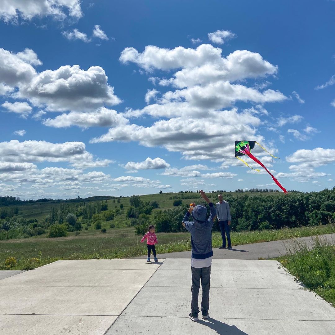 A boy flying a kite in a park with his sister and parent watching nearby.