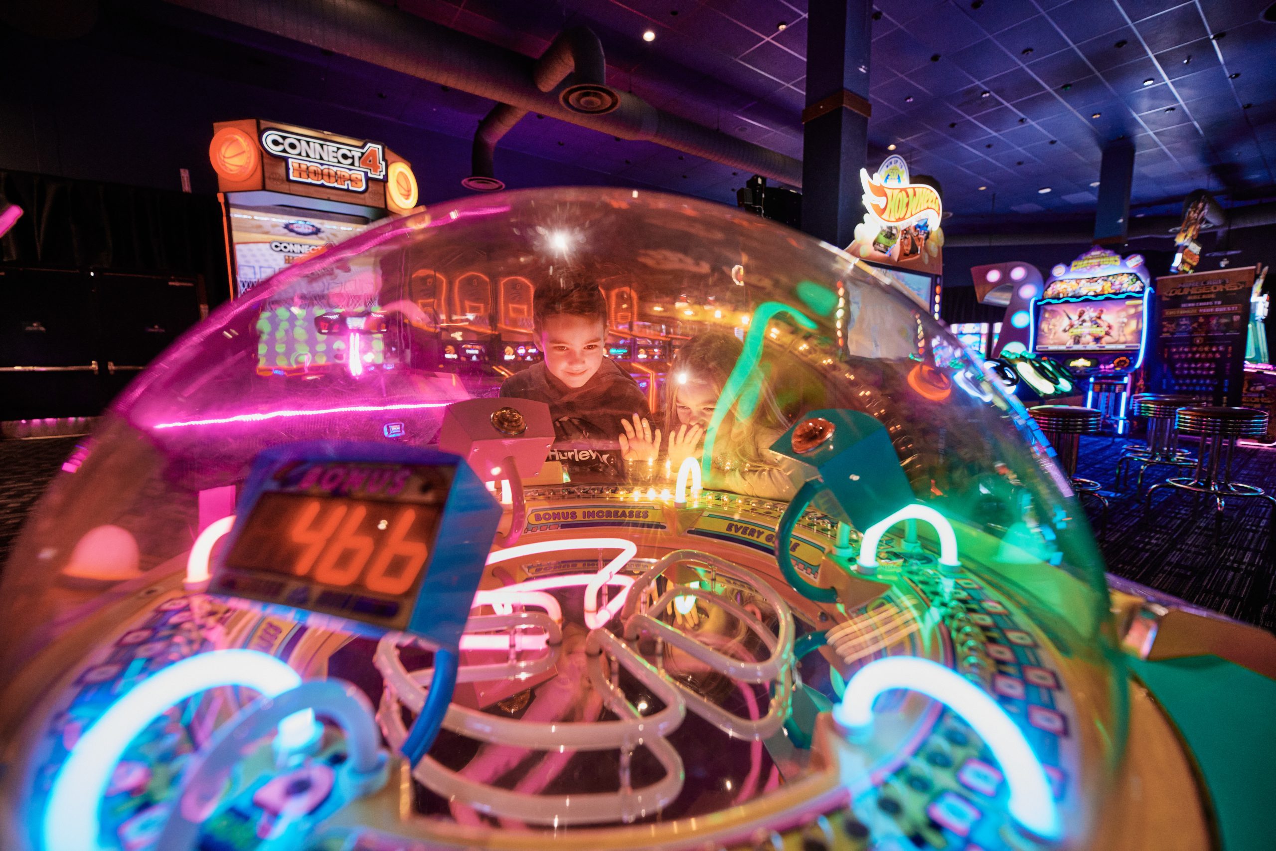 A young boy starting into a cylindrical arcade game with fluorescent lights.