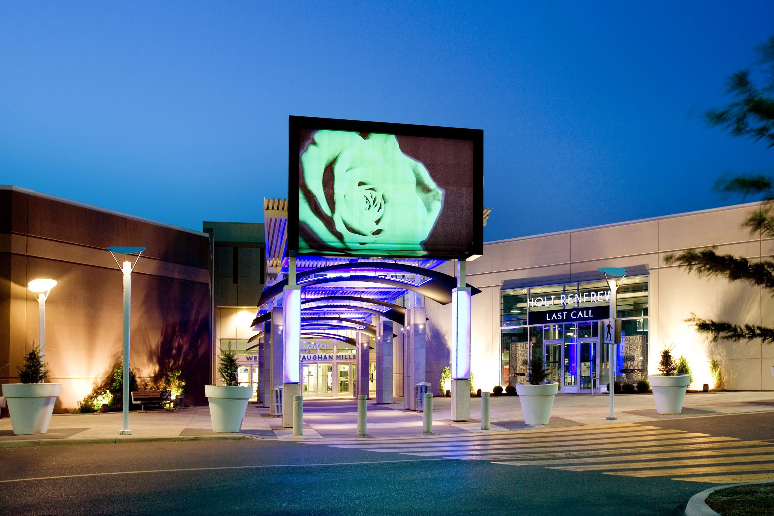 Entrance to a mall with pillars lit up in purple lighting and a large banner with a green flower on it.