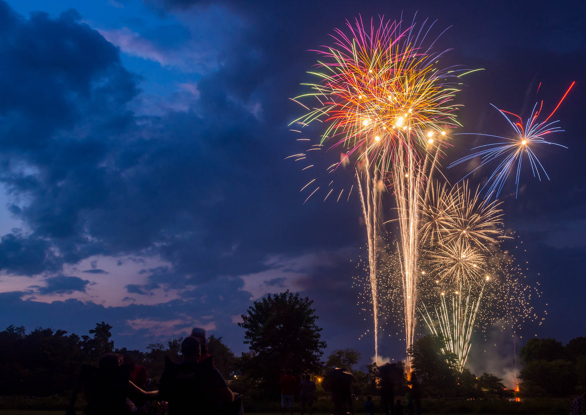 Lit up golden fireworks in a dark, cloudy sky.